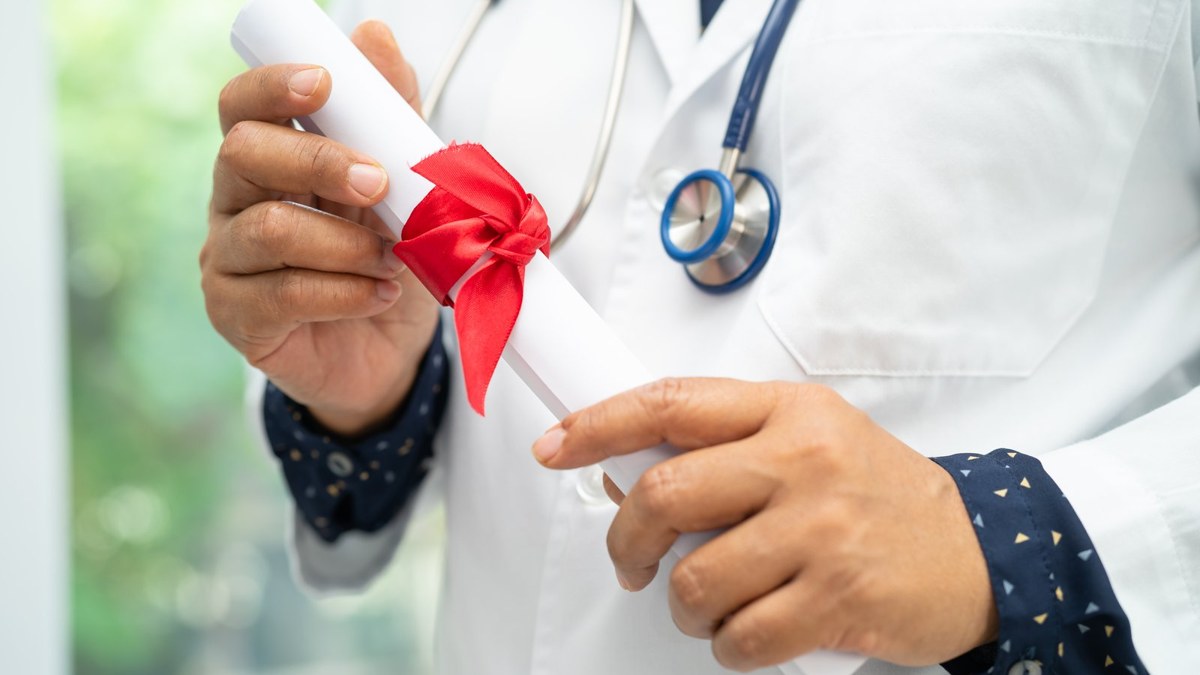 Medical graduate in a white coat holding a rolled MBBS diploma, representing BMDC registration for Bangladeshi doctors who studied abroad