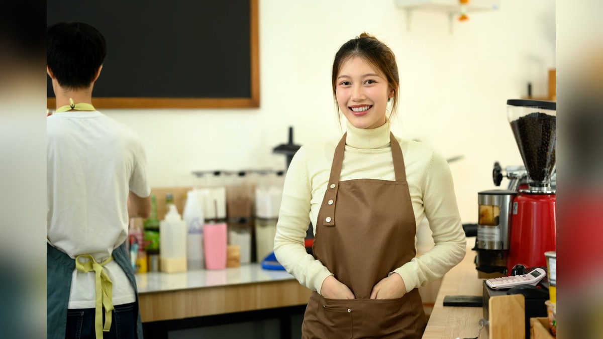 A student in an apron working a part-time shift behind a cafe counter in Japan