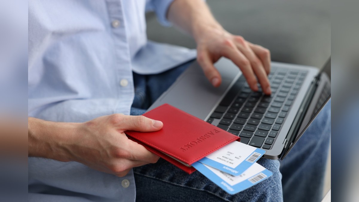 A traveller applying online for a Malaysia tourist visa with a passport and flight tickets beside a laptop