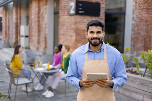 Bangladeshi student working part-time in a Malta cafe holding a tablet