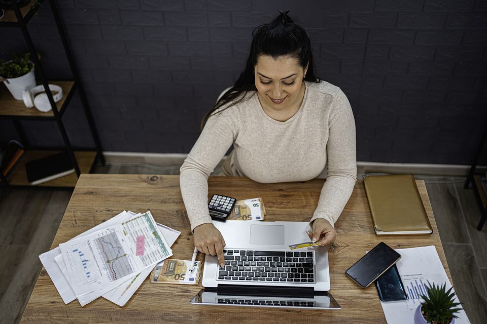 Mujer revisa sus gastos con calculadora y laptop antes de contratar un plan de hosting