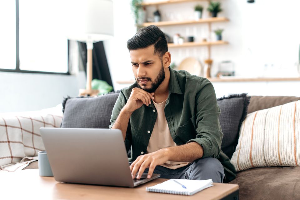 Hombre pensativo compara planes de hosting en su laptop desde la sala de su casa